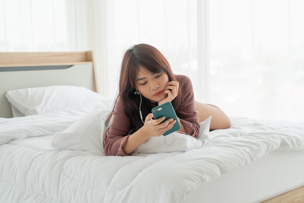 Asiatische Frau, die Smartphone auf Bett spielt