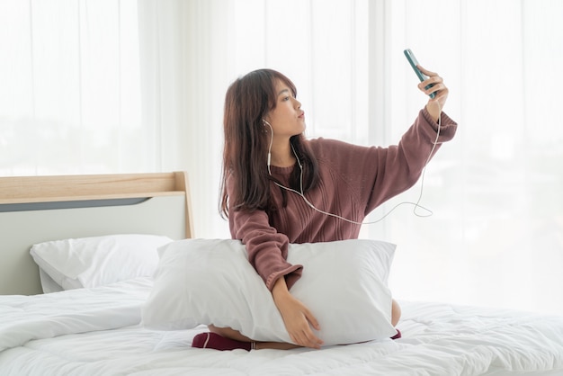 Asiatische Frau, die Smartphone auf Bett spielt