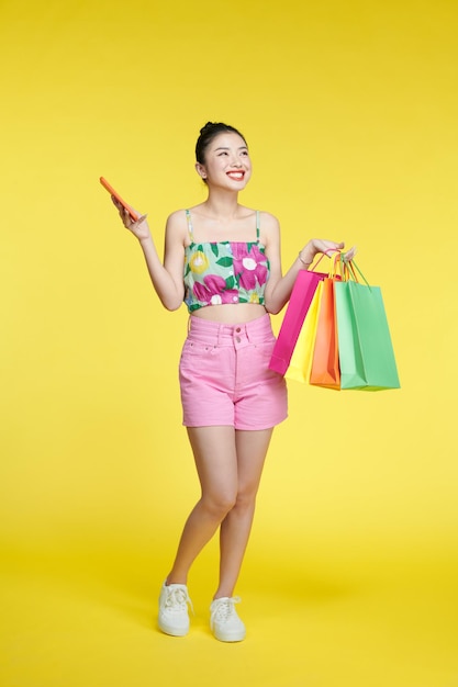 Asiatische Frau, die Taschen trägt und Handy im Studio hält, lokalisierte farbigen Hintergrund