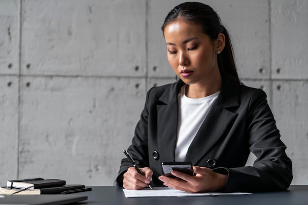 Asiatische Frau, die Telefon benutzt und am Tisch schreibt