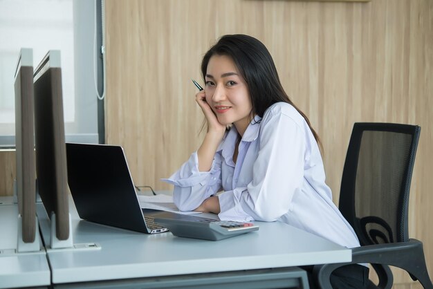 Asiatische frau, die überstunden im büro macht geschäft viel arbeitcheck-datei mit laptopthailand-leute mit bürouniform