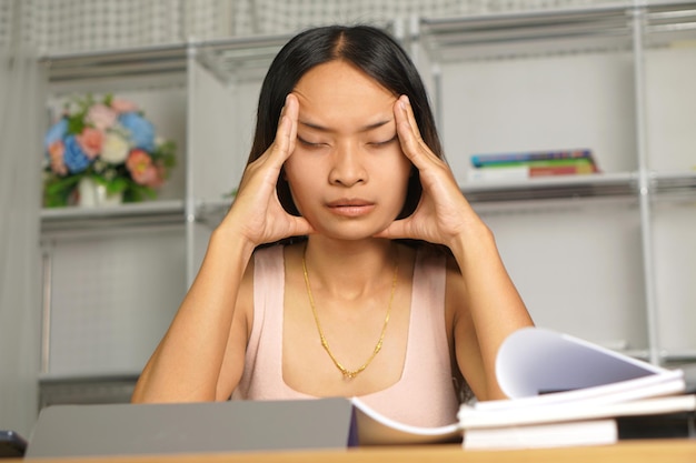 Asiatische Frau, die von zu Hause aus arbeitet, müde von Papierarbeit, die nicht pünktlich abgeschlossen wird