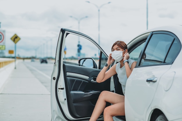 Asiatische Frau, die während der Ausgangssperre-Pandemie des Coronavirus Covid-19 im Freien eine schützende Gesichtsmaske trägt, bevor sie aus dem Auto steigt