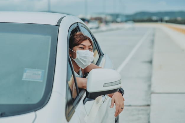 Asiatische Frau, die während der Ausgangssperre-Pandemie des Coronavirus Covid-19 im Freien eine schützende Gesichtsmaske trägt, bevor sie aus dem Auto steigt