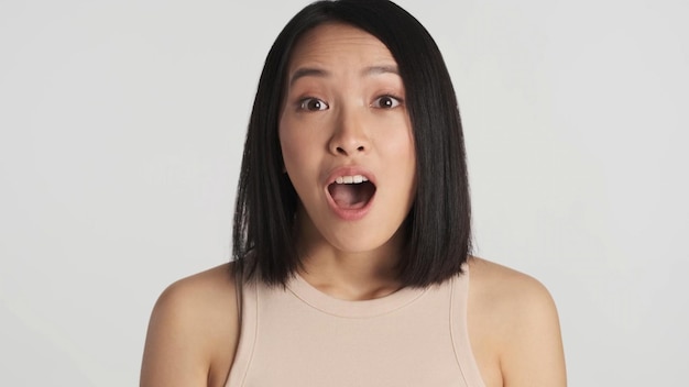 Asiatische Frau, die wegen guter Nachrichten mit offenem Mund in die Kamera schaut Wow-Ausdruck auf weißem Hintergrund