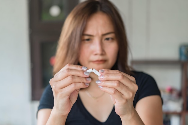 Asiatische Frau, die Zigarette mit der Hand zerdrückt, aus dem Suchtkonzept aussteigen, kein Tabaktag, kein Raucherkonzept