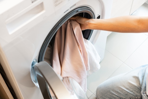 Asiatische Frau, die zu Hause Kleidung in die Waschmaschine in der Küche steckt. Wäschekonzept. Ansicht von oben