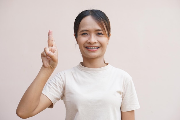 Asiatische Frau, die zwei gekreuzte Daumen hält