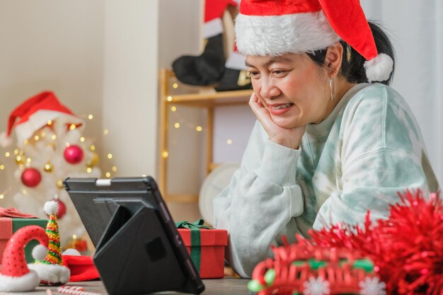 Asiatische Frau feiert Neujahr und Weihnachtsfeier mit Tablet-Videoanruf-Freunden zu Hause