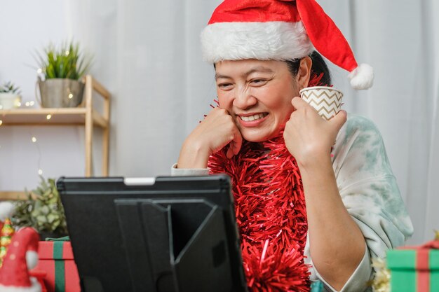 Asiatische Frau feiert Neujahr und Weihnachtsfeier mit Tablet-Videoanruf-Freunden zu Hause
