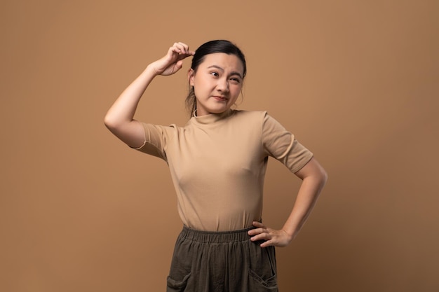 Asiatische Frau gelangweilt und verärgert, die sich am Kopf kratzt, isoliert auf beigem Hintergrund