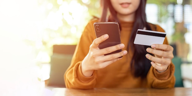 Asiatische Frau hält ein Smartphone und eine Kreditkarte, um online einzukaufen und ihre Bestellung zu bezahlen