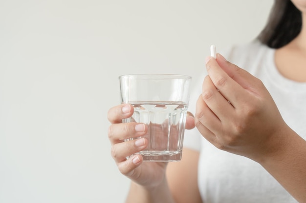 Asiatische Frau hautnah bereit, eine Ergänzungspille mit einem Glas Wasser einzunehmen