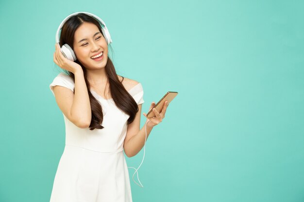 Asiatische Frau hört Musik mit Kopfhörern auf dem Handy isoliert auf grünem Hintergrund