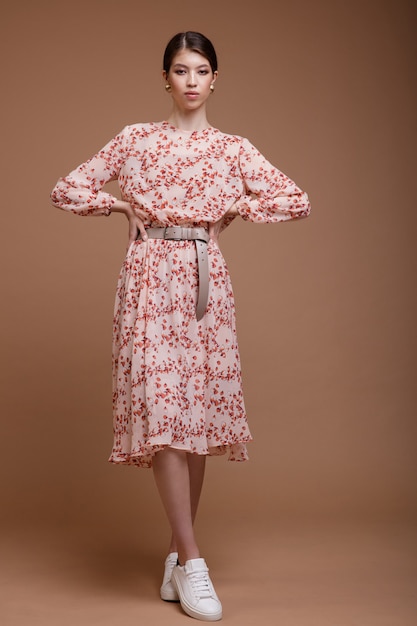 Asiatische Frau im beigen Kleid Blumenmuster posiert auf braunem Kaffee Hintergrund Studio Shot Portrait