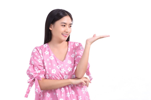 Asiatische Frau im rosa Kleid zeigt ihre Hand, um etwas auf weißem Hintergrund zu präsentieren.