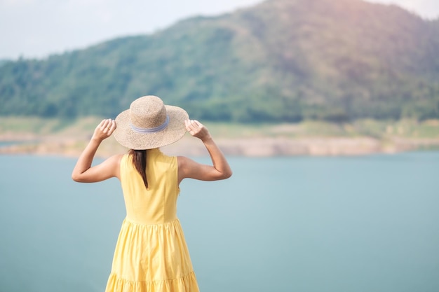 Asiatische Frau in gelbem Kleid und Hut Reisen im Freien Glücklicher Reisender mit Blick auf den Khun dan Prakarnchon Damm, Wahrzeichen und beliebt für Touristenattraktionen in Nakhon Nayok Thailand