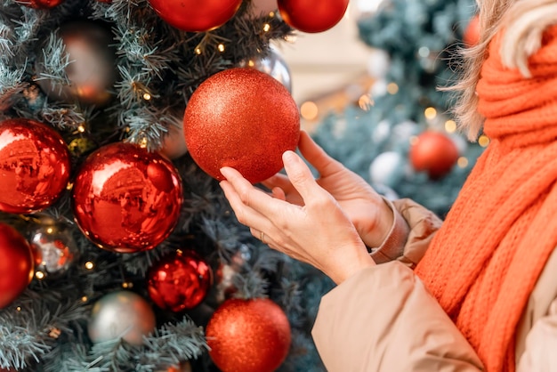 Asiatische Frau in orangefarbenem Schal und Hut, die auf dem mit Weihnachtslichtern geschmückten Weihnachtsmarkt spazieren geht