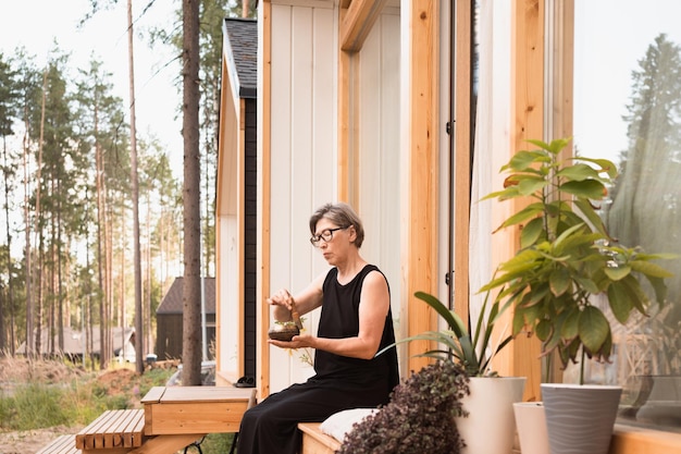 Asiatische Frau in schwarzem Kleid sitzt auf der Terrasse des Landhauses mit Klangschale