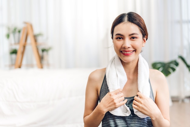 asiatische Frau in Sportkleidung, die nach Yoga zu Hause mit einem Handtuch auf den Schultern sitzt