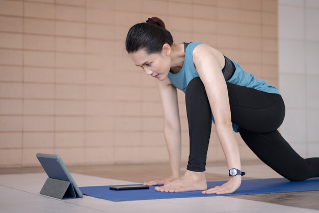 Asiatische Frau in Sportoutfits trainiert nach Online-Trainingsprogramm über ein digitales Tablet zu Hause