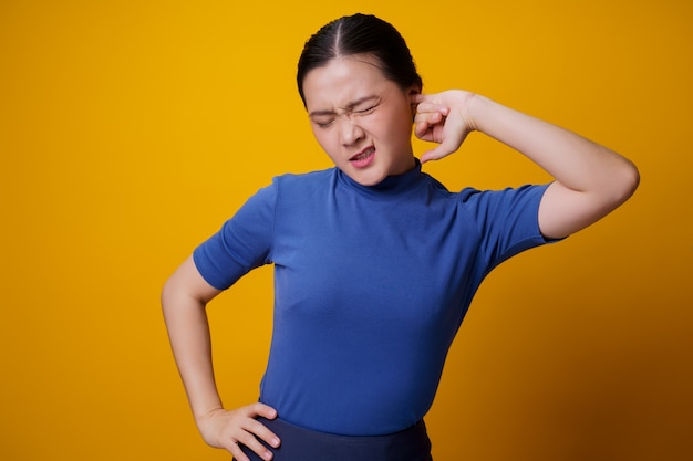 Asiatische Frau juckt und steckt einen Finger in ihre Ohren, der über gelb steht.