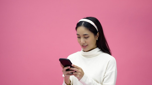 Asiatische Frau lächelt und benutzt Handy mit Tablet und freut sich auf Online-Shopping auf isoliertem rosa Hintergrund