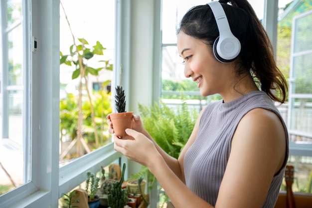 Asiatische Frau lächelt und schaut auf die Pflanze im Garten für einen entspannten Tag zu Hause. Sie trägt Kopfhörer zum Musikhören