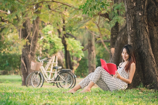 Asiatische Frau lebt im Park im Freien, liest ein Buch und hört Musik für Entspannung und Glück im Sommer