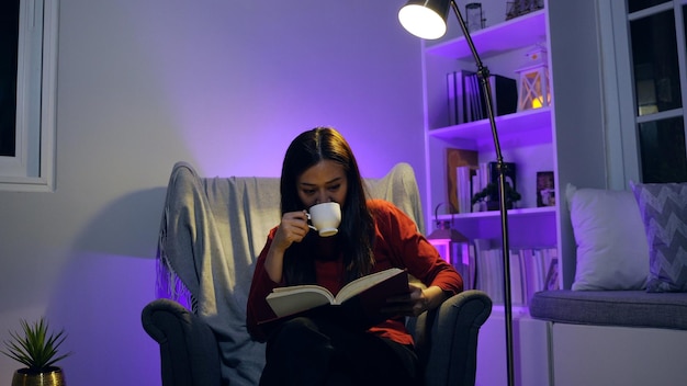 Asiatische Frau liest Buch nachts im Wohnzimmer. Lifestyle und Entspannung zu Hause.
