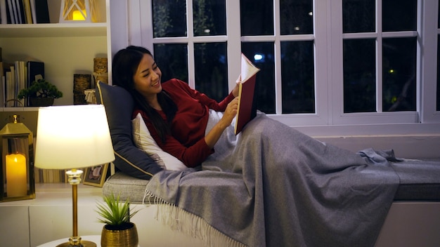 Asiatische Frau liest Buch nachts im Wohnzimmer. Lifestyle und Entspannung zu Hause.