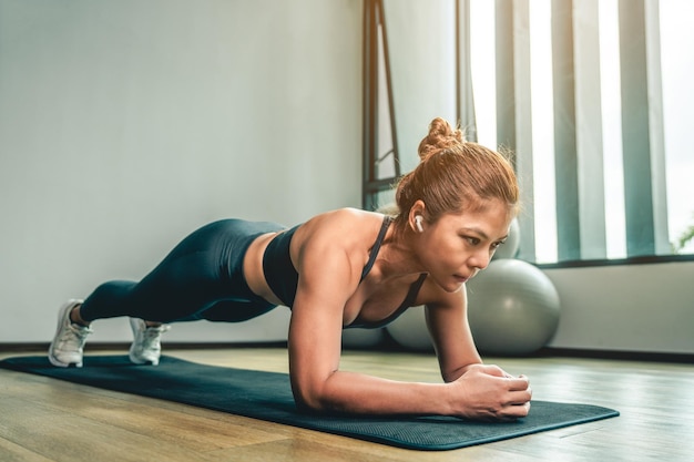 Foto asiatische frau macht yoga-plank auf einer yogamatte im fitnessstudio und trainiert drinnen während der quarantäne. übungstraining und fitness-lifestyle-konzepte