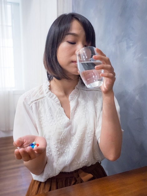 Asiatische Frau mit einem Glas Wasser und Pillen