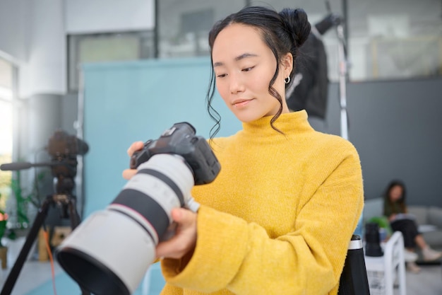 Asiatische Frau mit Fotokamera und Mitarbeiter einer digitalen Agentur überprüfen Bilder in einem Studio Produktionsprozess des Fotografen und professionelles Fotoshooting mit einem kreativen Mitarbeiter, der die Katalogergebnisse überprüft