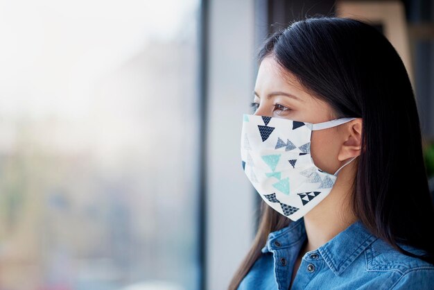 Asiatische Frau mit Gesichtsmaske schaut durch das Fenster