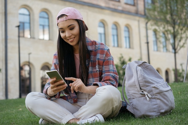 Asiatische Frau mit Handy auf Gras sitzend