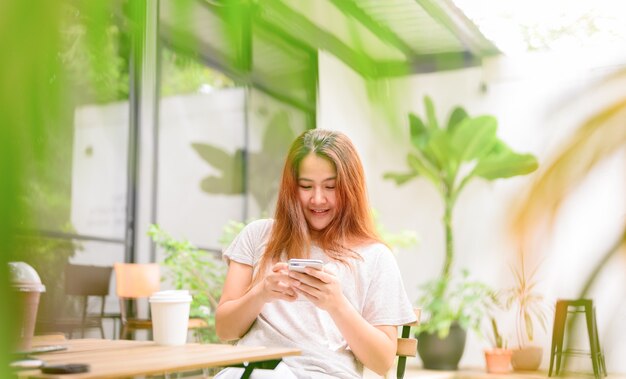 Asiatische Frau mit Handy und Kaffee allein. Entspannung und Erholung im Botanischen Garten im Urlaub.