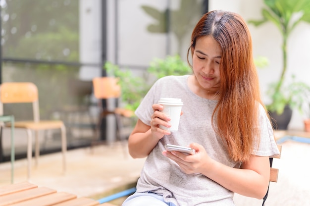 Asiatische Frau mit Handy und Kaffeetrinken allein. Entspannung und Erholung im Botanischen Garten im Urlaub.