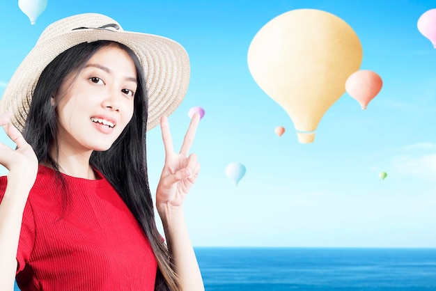 Asiatische Frau mit Hut und buntem Luftballon, der mit blauem Himmelshintergrund fliegt