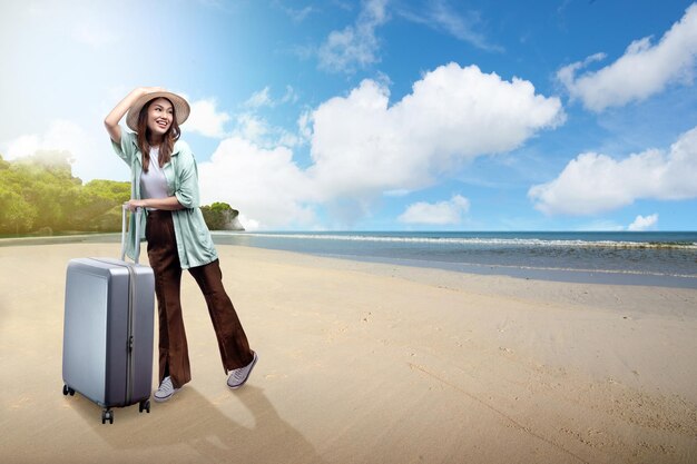 Asiatische Frau mit Hut und Koffer am Strand