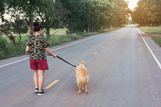 Asiatische Frau mit ihrem Golden Retriever-Hund, der auf der öffentlichen Straße geht.