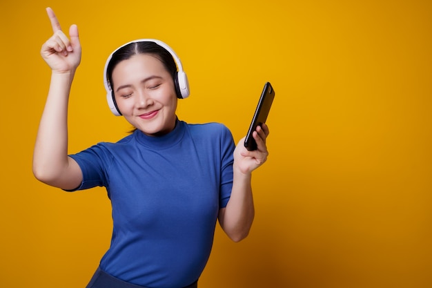 Asiatische Frau mit Kopfhörern, die Musik vom Smartphone auf Gelb hören.