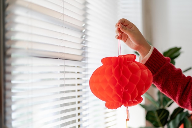 Asiatische Frau mit roter chinesischer Neujahrslaterne, während sie dekoriert flach den traditionellen Anhänger der chinesischen Neujahrsfeiern für viel Glück setzt. Chinesisches Wort bedeutet Segen