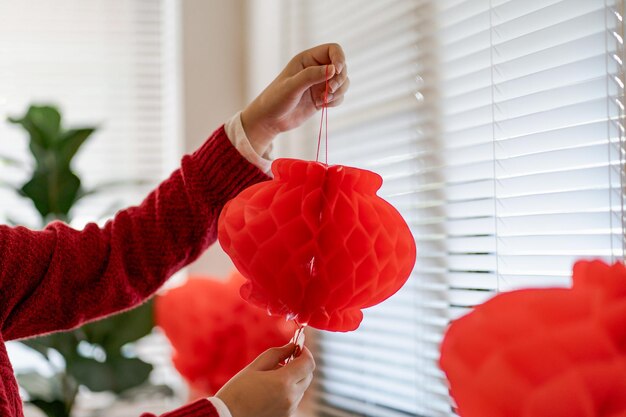 Asiatische Frau mit roter chinesischer Neujahrslaterne, während sie den traditionellen Anhänger flach dekoriert