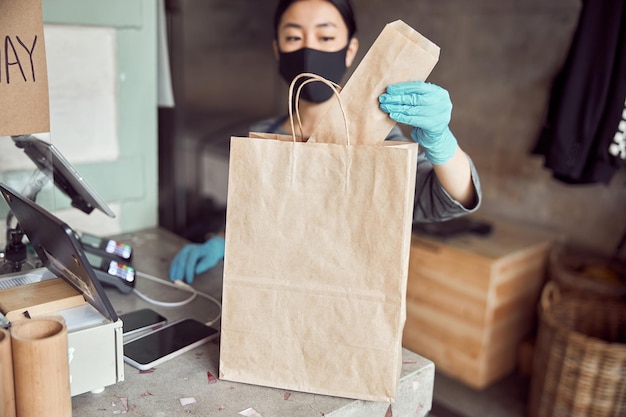 Asiatische Frau mit Schutzmaske und Handschuhen beim Servieren von Speisen zum Mitnehmen im städtischen Café während der Sperrung wegen Coronavirus-Pandemie