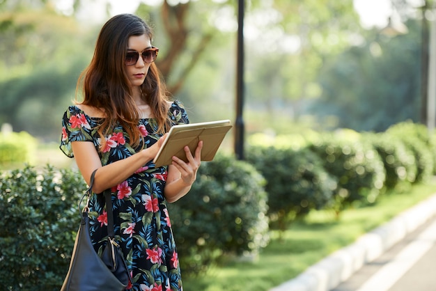 Asiatische Frau mit Tablette in der Nähe von Büschen