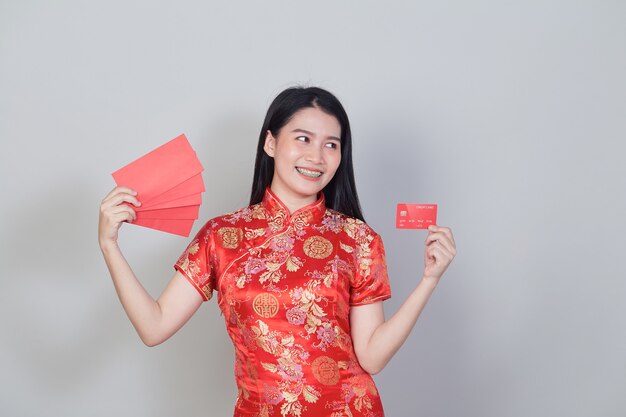 Asiatische Frau mit traditionellem Cheongsam-Qipao-Kleid mit Kreditkarte und roten Umschlägen für chinesische Neujahrs-Shopping-Konzepte.