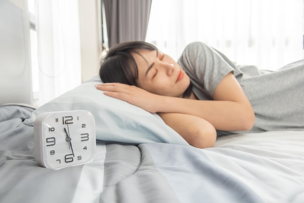 Asiatische Frau schläft auf dem Bett und entspannt sich mit einer Uhr