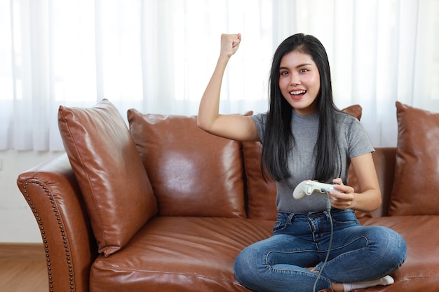 asiatische Frau sitzt auf dem Sofa, hält Joystick und spielt Spiel.