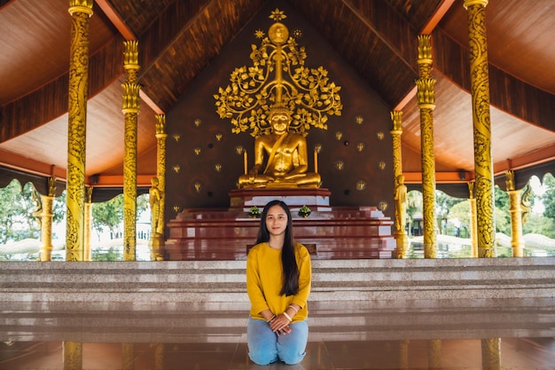 Asiatische Frau sitzt Meditation und goldene Buddha-Statue in der buddhistischen Kirche im Wat Sirindhorn wararam